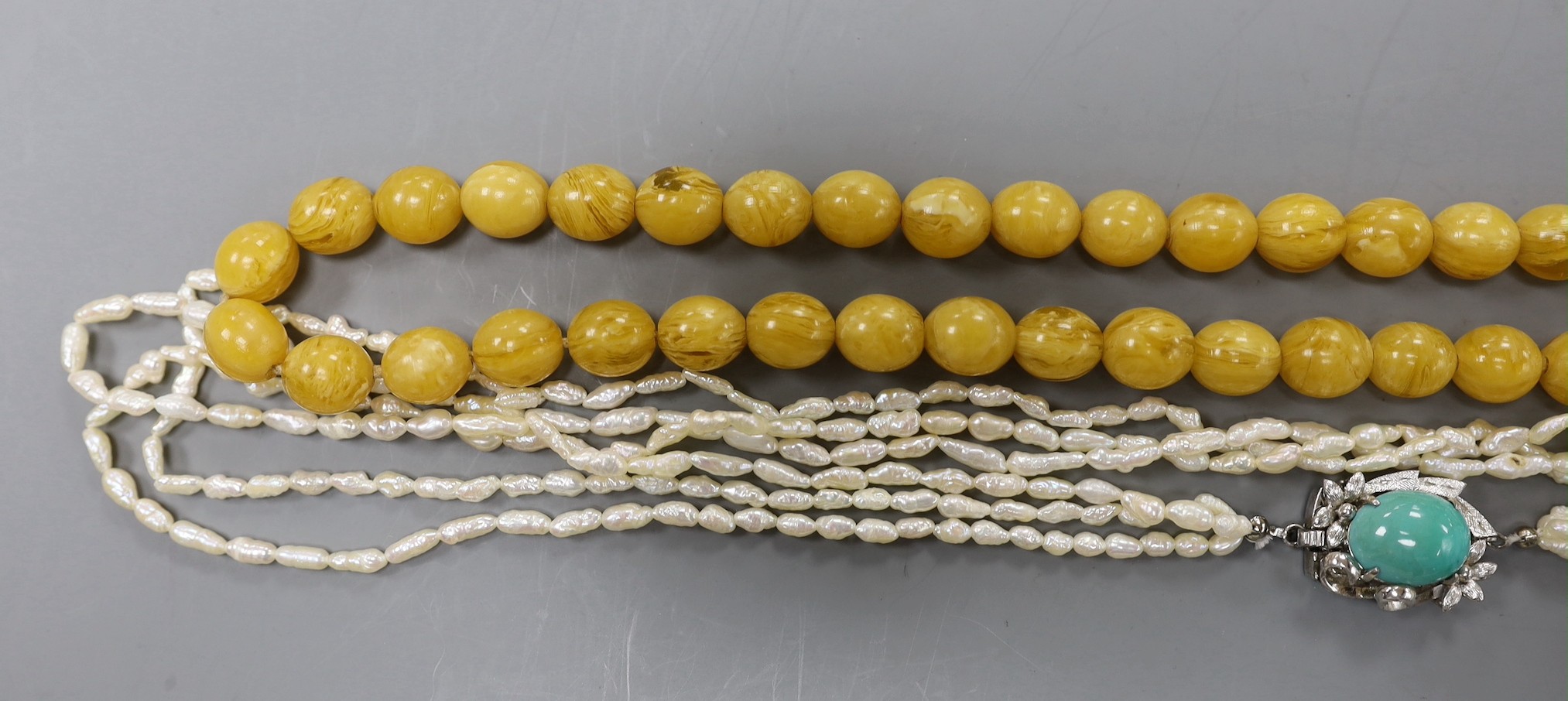 A multi-strand 'rice pearl' necklace with 18k white metal and turquoise set clasp, 66cm and an amber necklace.